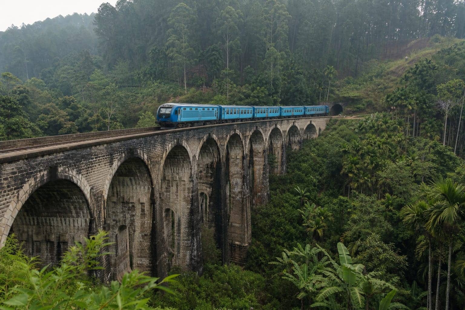 A blue train crossing the nine stone arches of the Demodara viaduct near Ella, Sri Lanka
