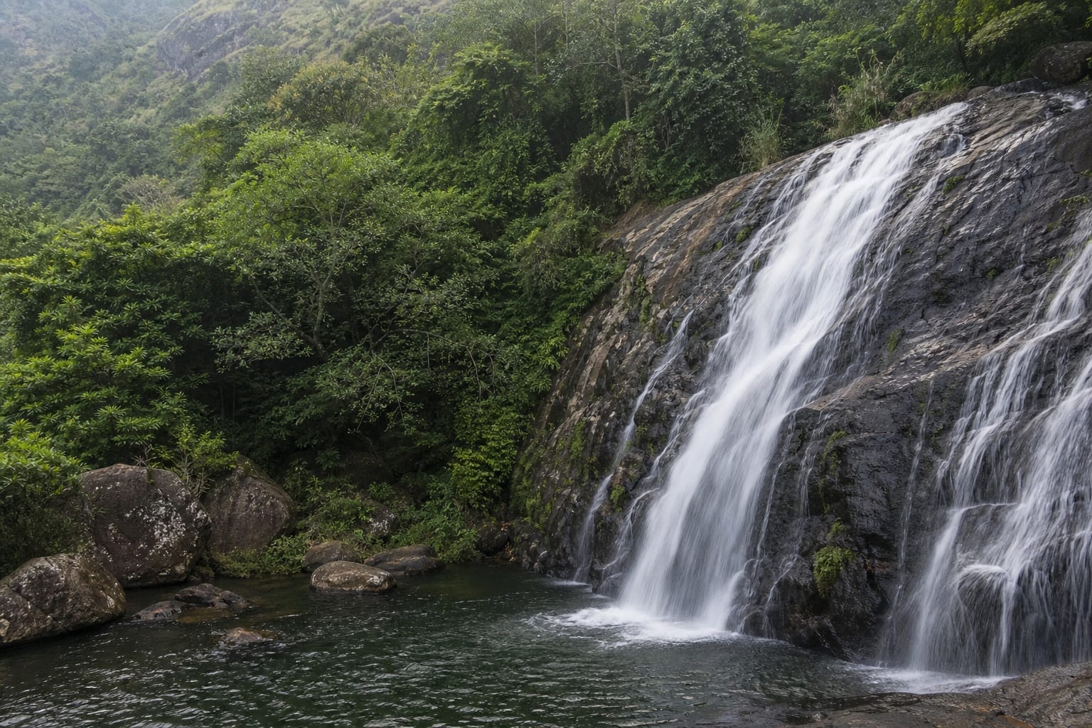 Water falling over dark rock into a forest pool in the Sri Lankan hill country