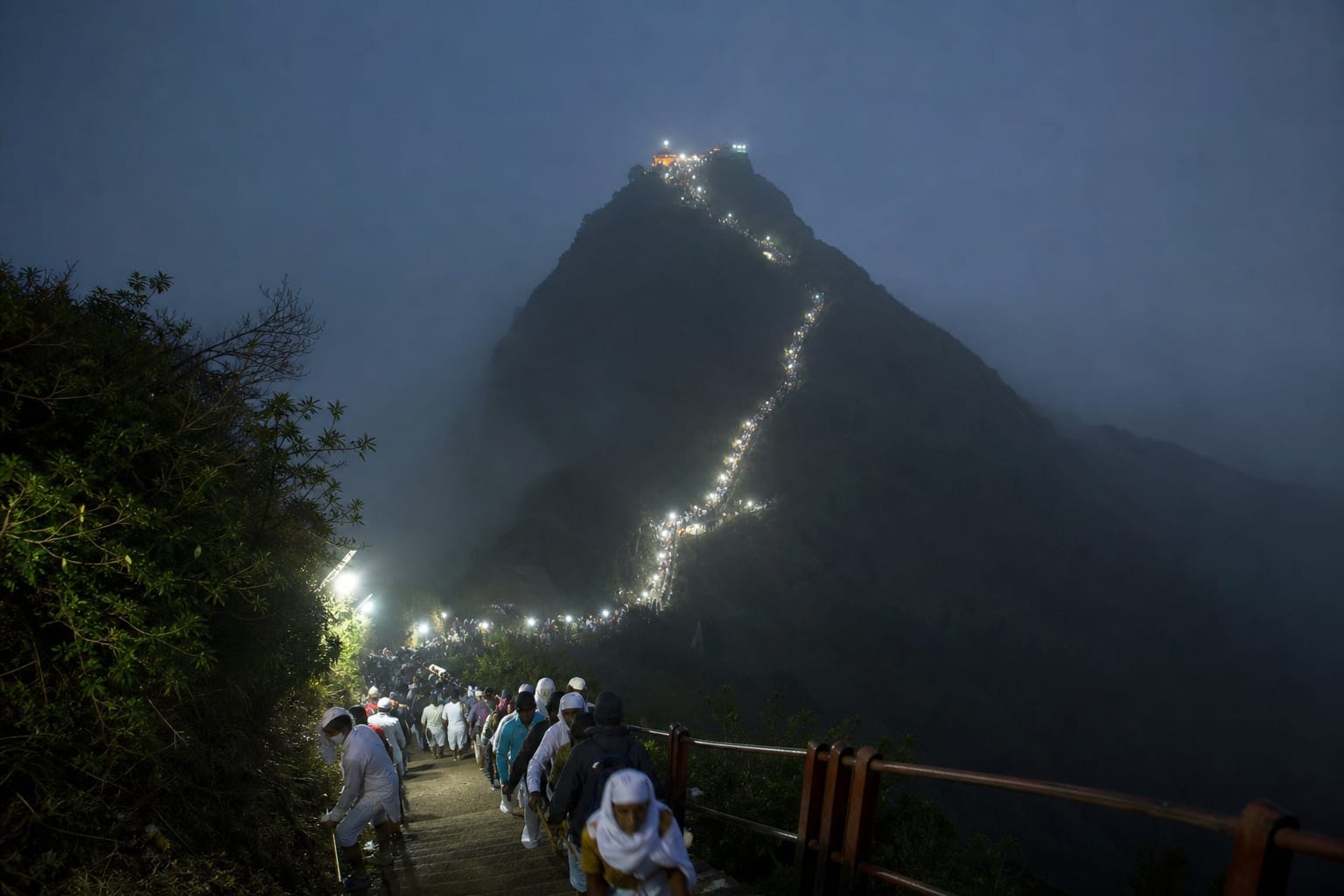 The lit pilgrimage stairway winding up Adam's Peak at night with pilgrims climbing