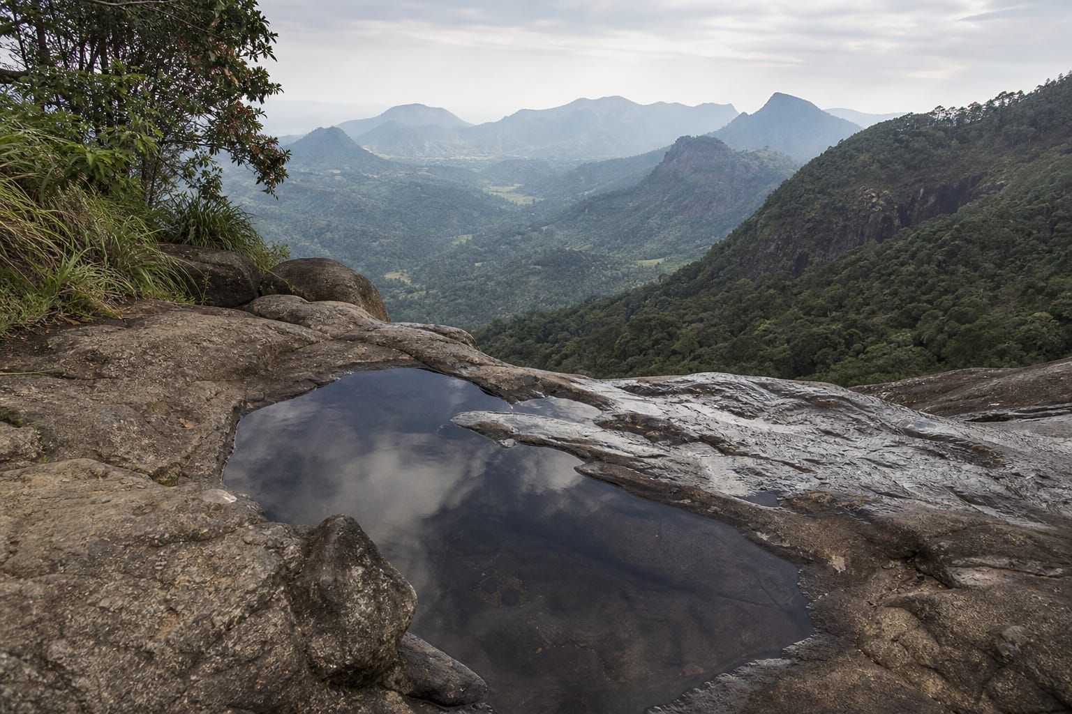 Natural rock pools at the head of a waterfall looking out over a valley in Uva province